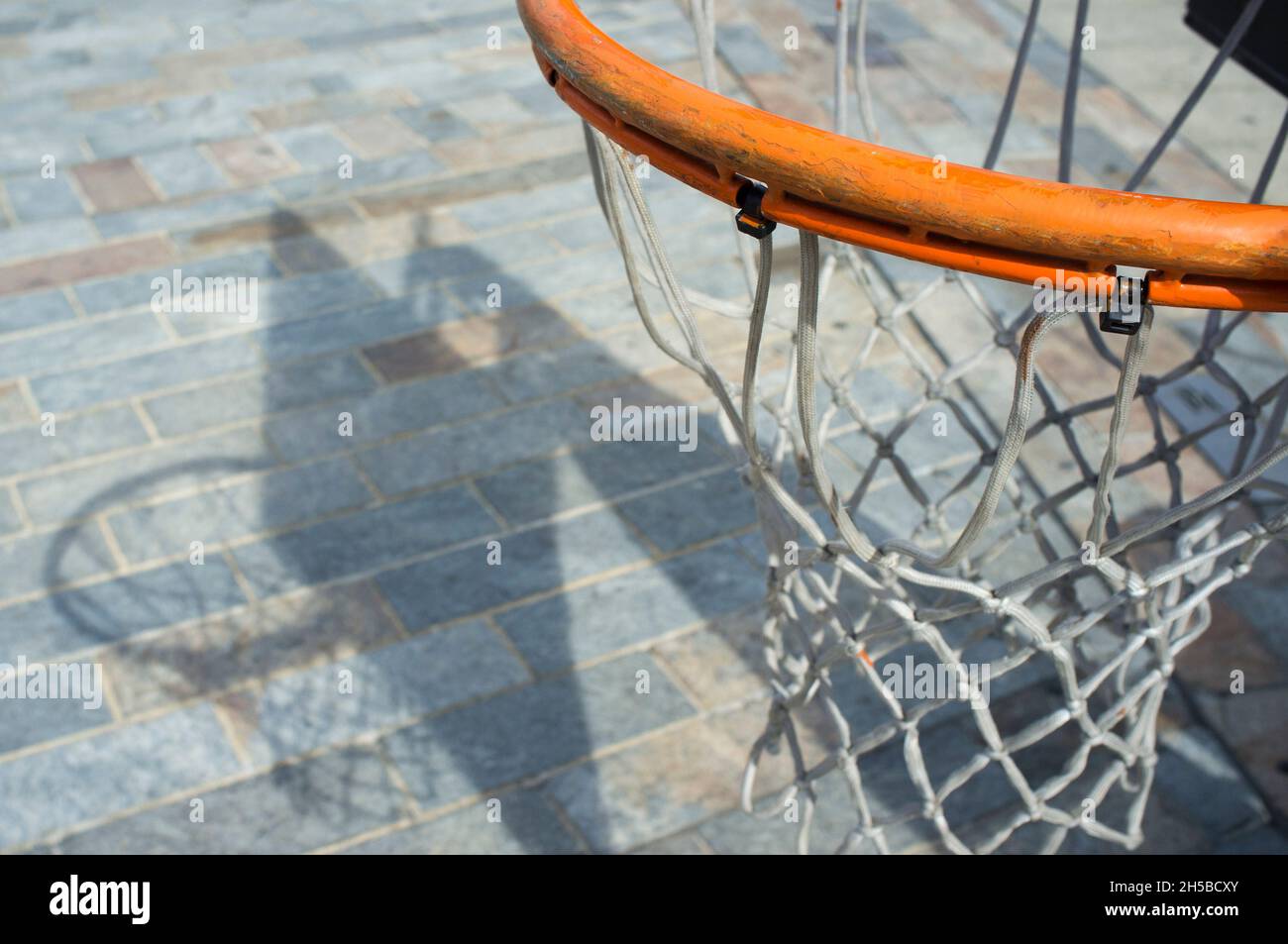 Basketball hoop proyecting shadow over cobble stone road surface