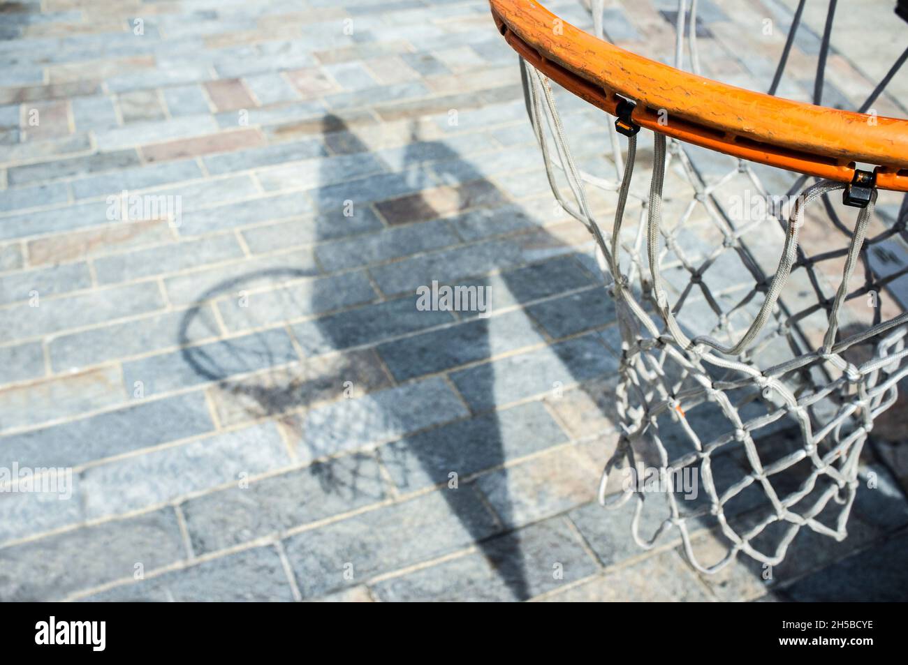 Basketball hoop proyecting shadow over cobble stone road surface