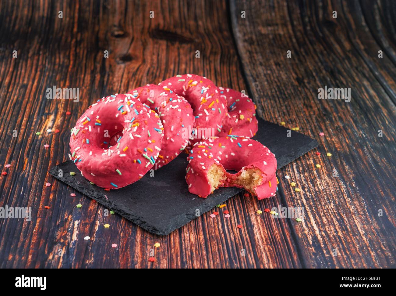 Stack of pink donuts decorated with colorful sprinkles on a black stone-plate Stock Photo