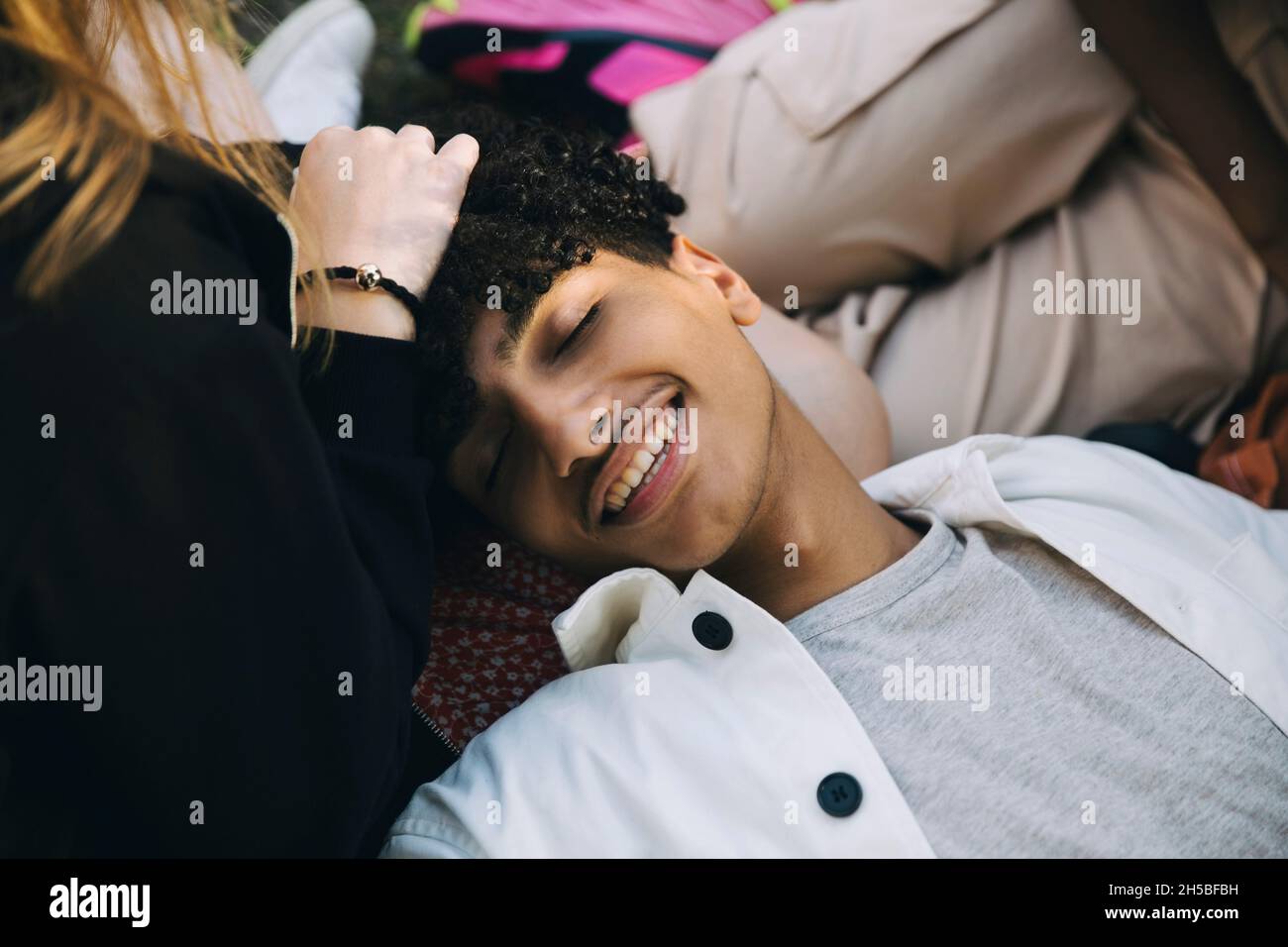 Smiling teenage boy lying with head on lap of female friend Stock Photo