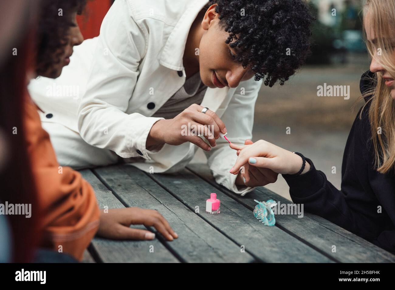 Male teenager applying nail polish to female friend at table Stock Photo