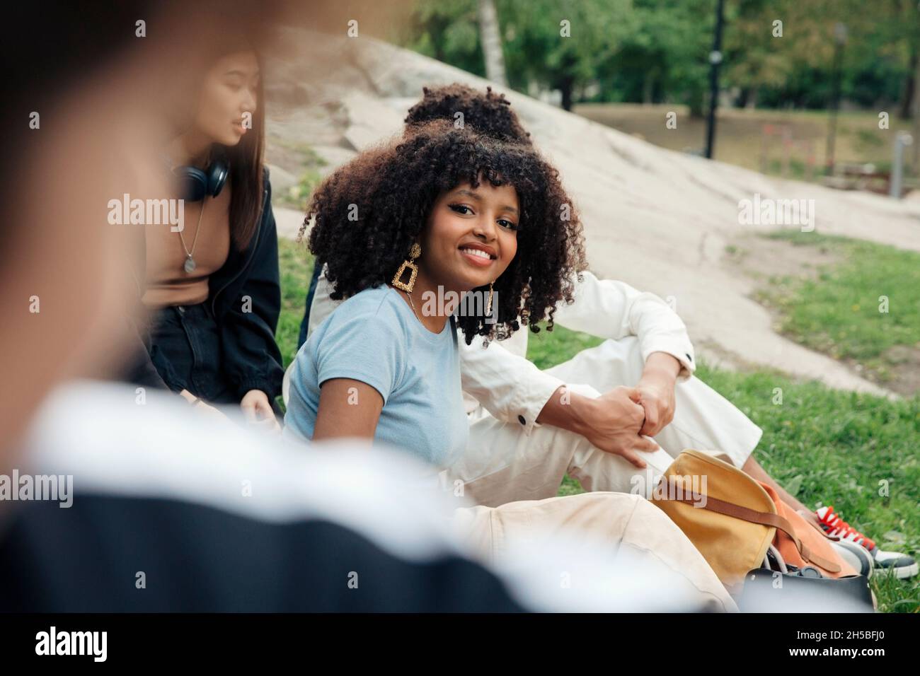 Smiling teenage girl sitting with male and female friends in park Stock Photo