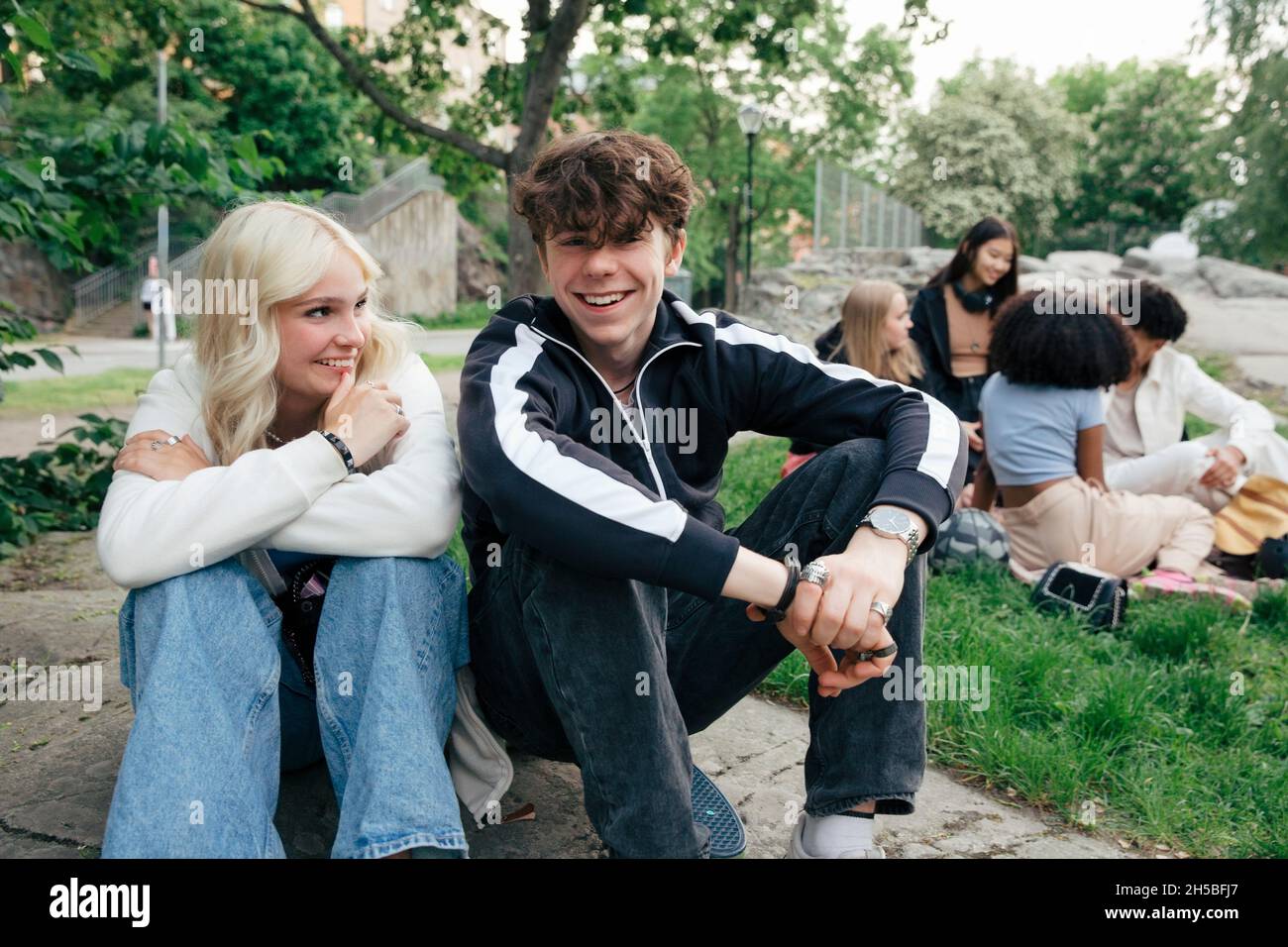 Portrait of smiling teenage boy sitting by blond girl with friends in background Stock Photo