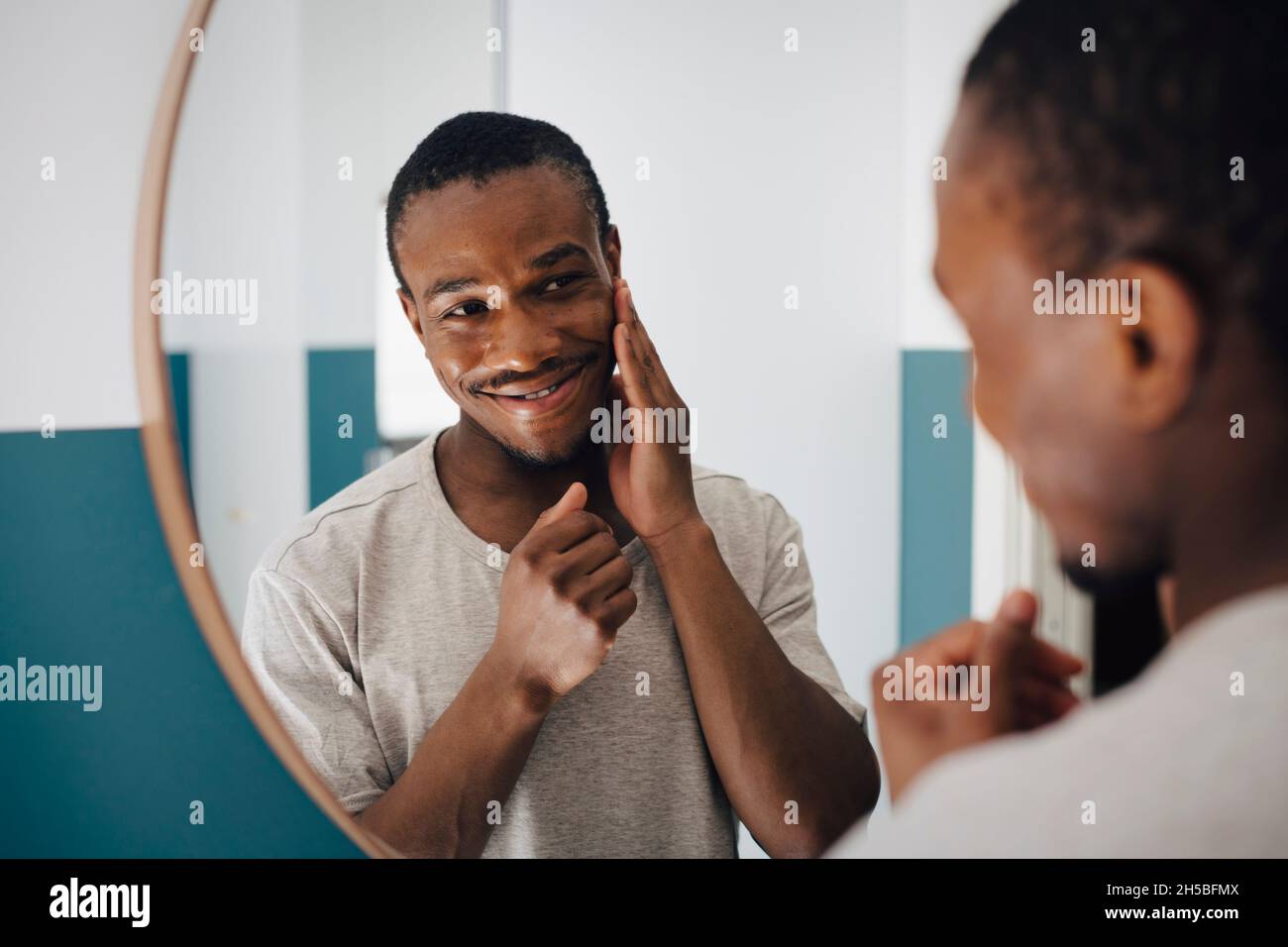 Smiling man touching face while looking in mirror at home Stock Photo