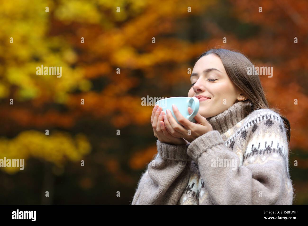 Happy woman in autumn smelling coffee holding mug in a park Stock Photo