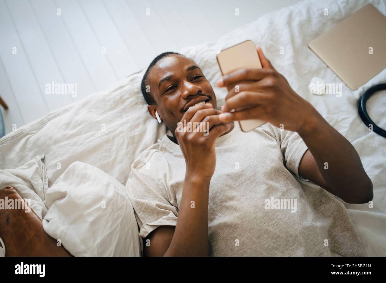 Smiling mid adult man using mobile phone while lying on bed Stock Photo