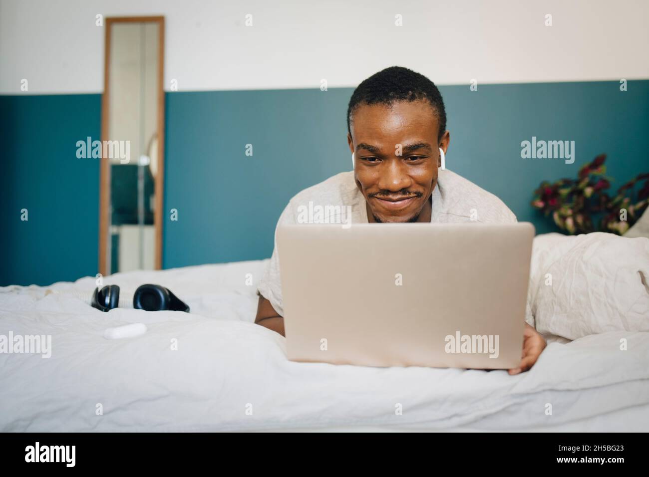 Smiling mid adult man using laptop while lying on bed at home Stock Photo