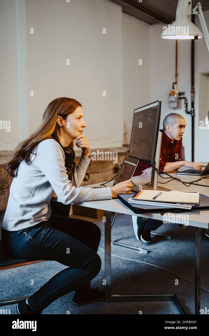 Mature female programmer coding over computer and laptop in startup company Stock Photo