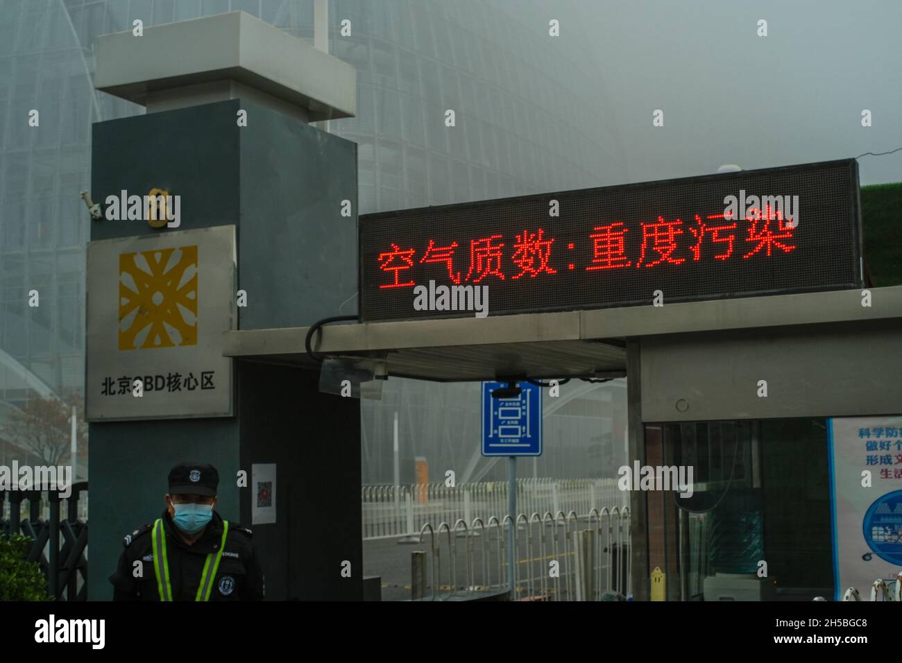 Chinese characters on the LCD screen: Air quality: heavy pollution. A man guards a tower shrouded by heavy smog in Beijing, China. 06-Nov-2021 Stock Photo