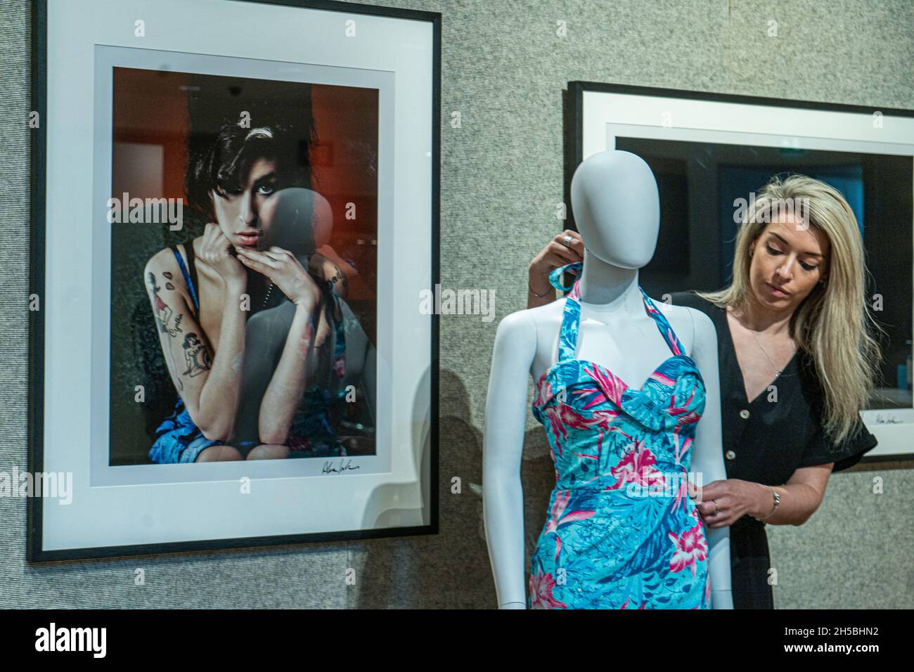 NEW BOND STREET LONDON, UK. 8 Nov, 2021. A member of staff adjusts a dress signed and worn by Amy Winehouse (Estimate: £30,000-40,000 ) in front of two photographs of Amy by Alex Lake at the Bonhams Pop X Culture Sale. The sale takes place on 17 November at Bonhams Knightsbridge. Stock Photo