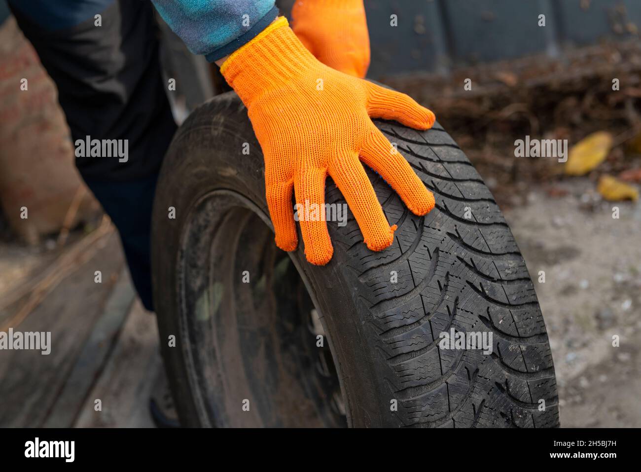 Winter tyre replacement. Car mechanic hands in safety gloves holding winter tyre. car preparation for winter season concept Stock Photo