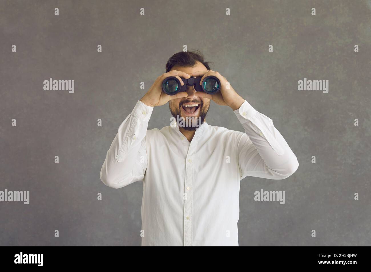 Young man looking through binoculars over grey studio background with happy face Stock Photo