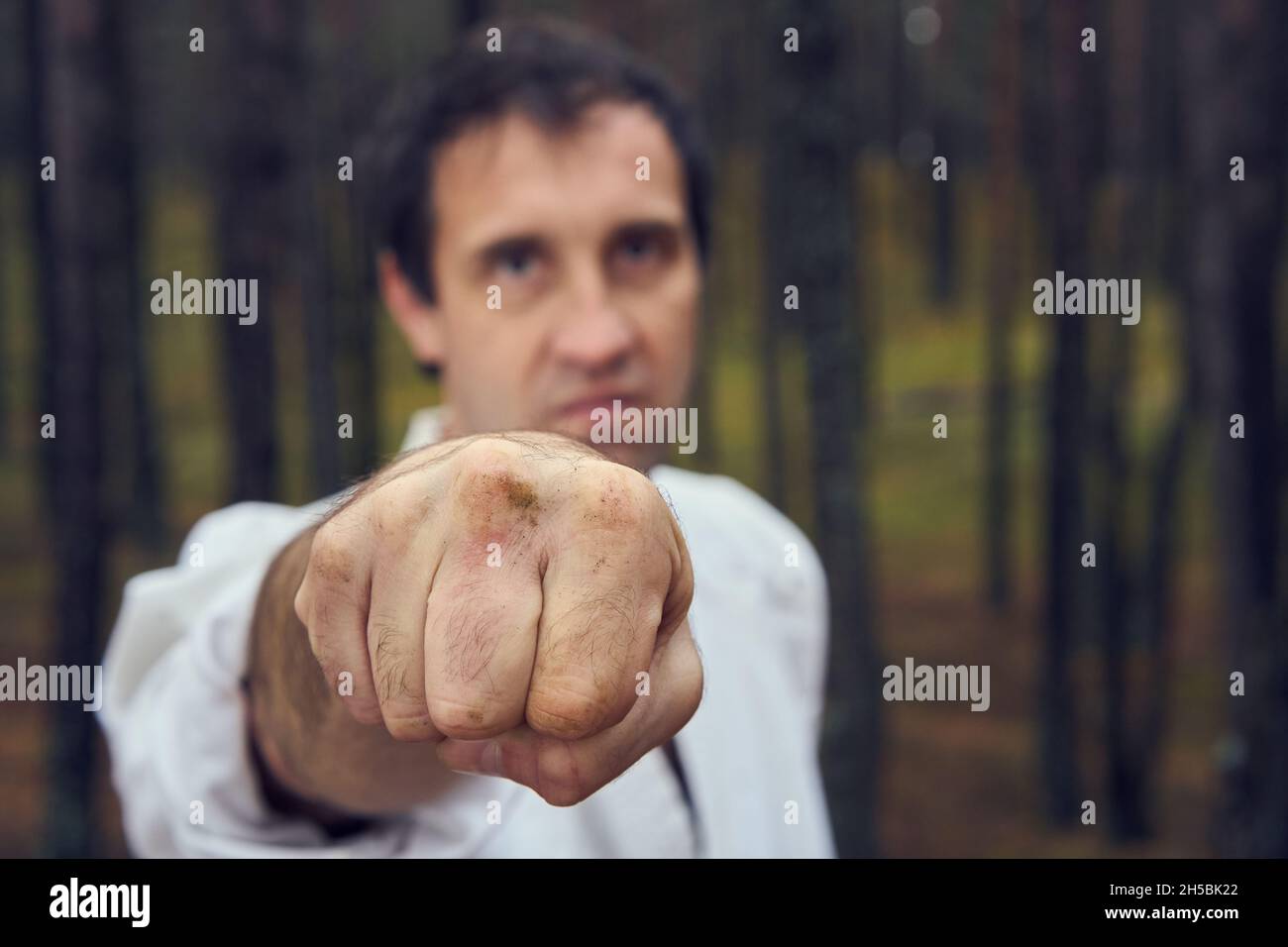 Karate man in an old kimono and black belt training punch at the forest