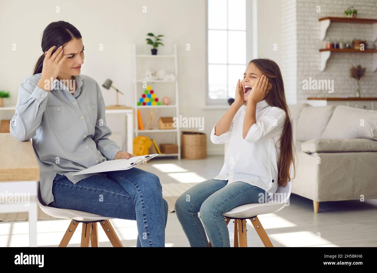Angry naughty child throwing tantrum during session with therapist or psychologist Stock Photo