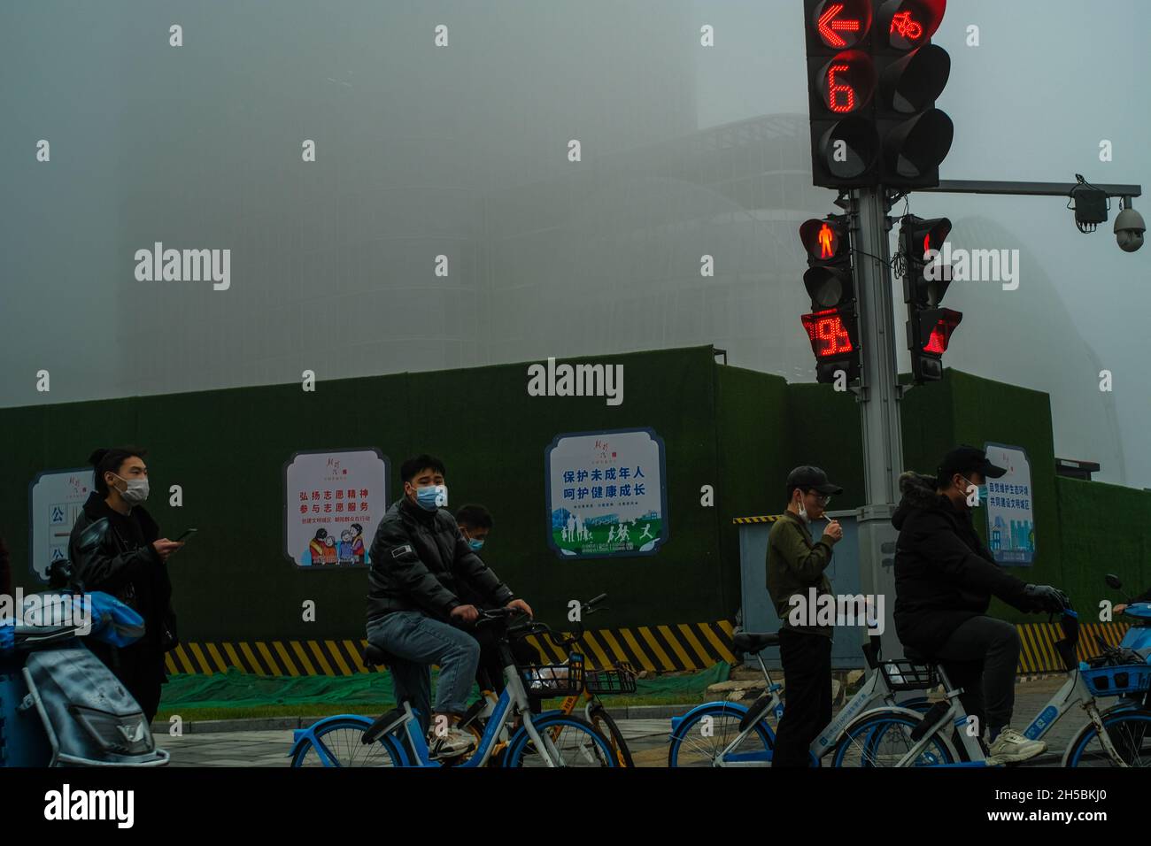 People ride bicycles past high-rise buildings in Beijing's central business district shrouded by heavy smog in Beijing, China. 06-Nov-2021 Stock Photo