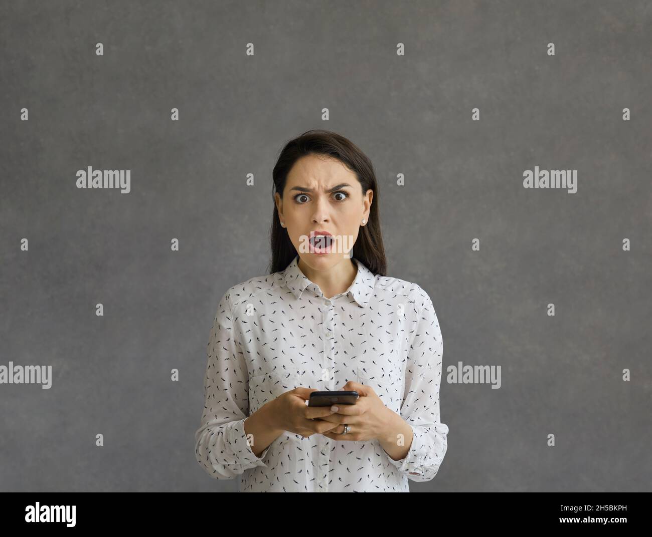 Frustrated and angry woman with dissatisfied facial expression stands with phone in hands. Stock Photo