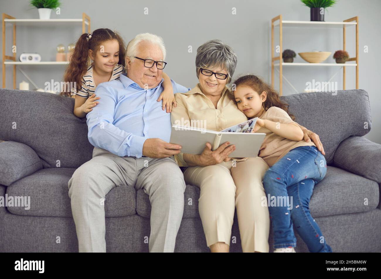Happy grandparents and their two granddaughters look at a photo book with a family photo together. Stock Photo