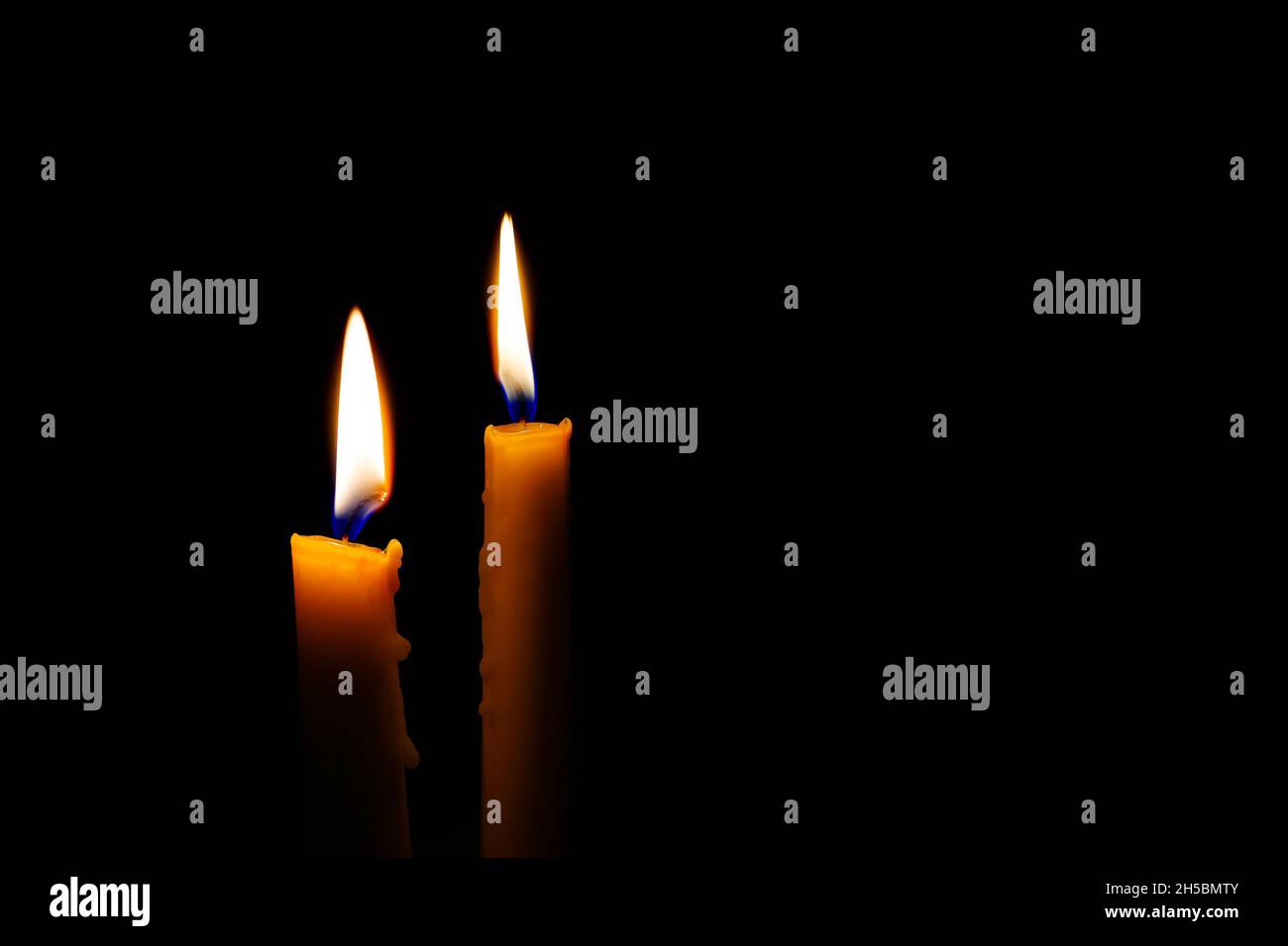 Two burning candles in the darkness. Burning yellow candles on black