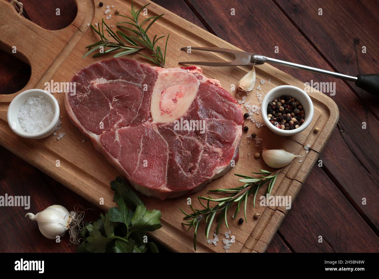 Raw fresh ossobuco con with herbs on wooden cutting board. Braised veal meat. Directly above. Stock Photo