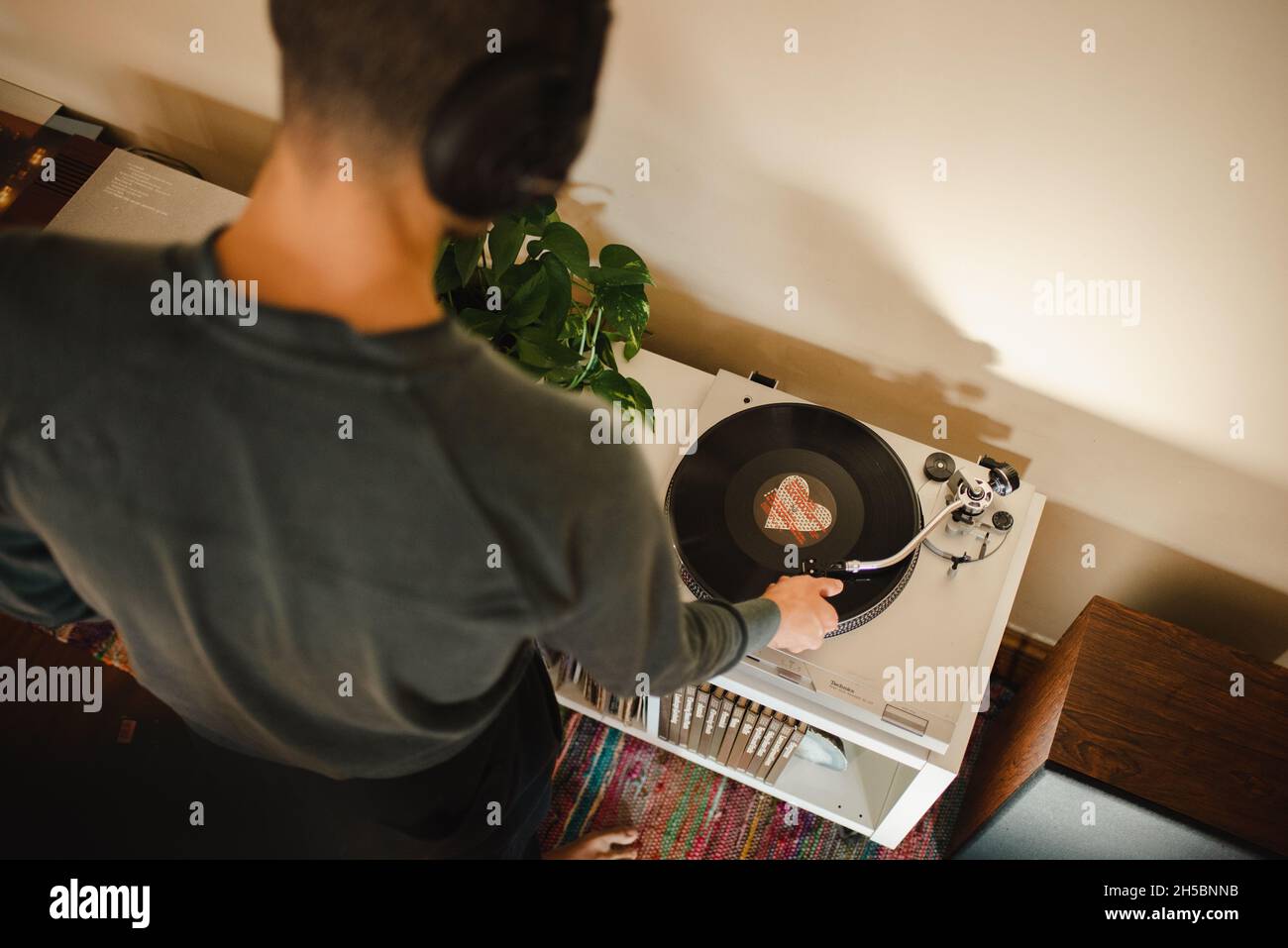 Young millennial mixed-race man puts needle on vinyl record, listening to music with headphones on in his apartment. Aerial view oflistening to music Stock Photo