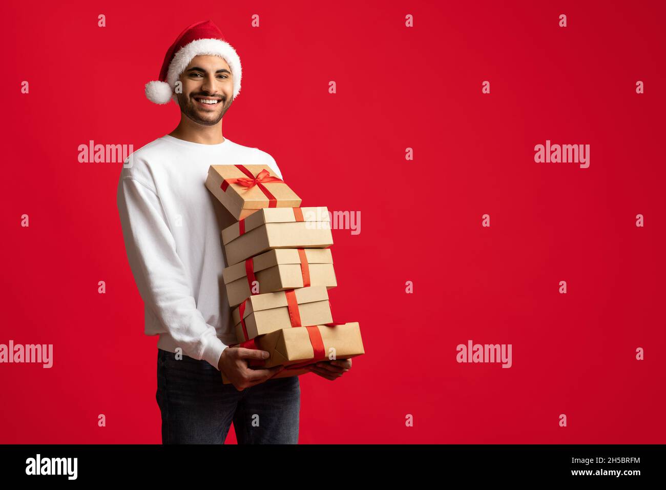 Merry Christmas. Happy Arab Man In Santa Hat Holding Many Gift Boxes Stock Photo