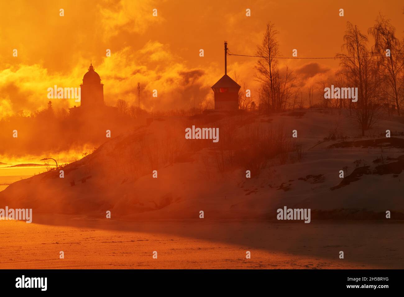 Blazing morning sunrise behind small beacon or lighthouse on the rocky island in front of Suomenlinna fortress island on an extremely cold winter morn Stock Photo