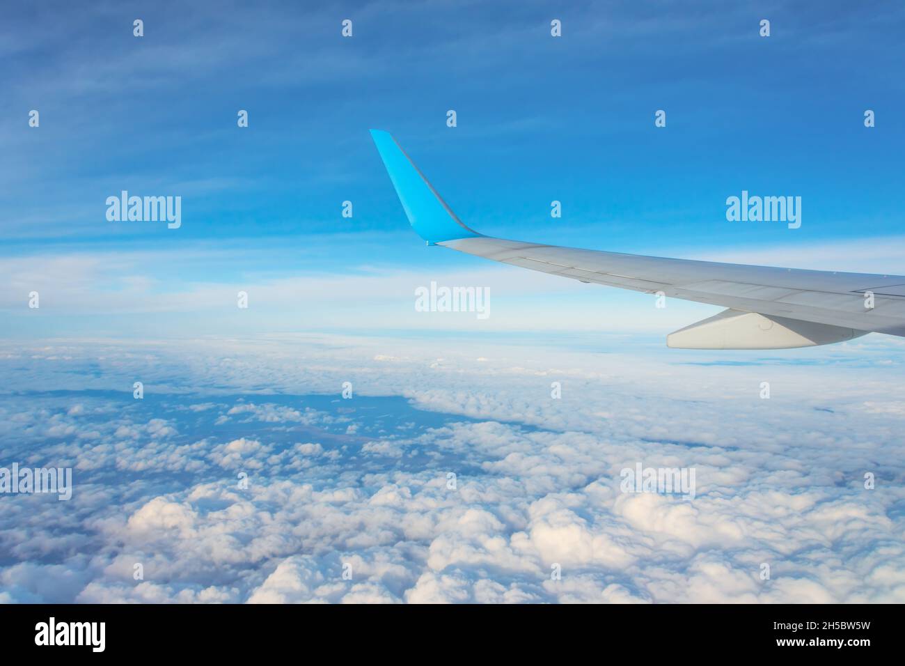 Wing of an airplane flying above the clouds. Looks at the sky from the window of the plane, using airtransport to travel Stock Photo