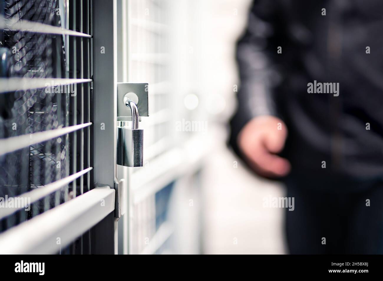 Burglar or thief and storage with lock in basement of condo apartment building. Suspicious man, intruder and criminal. Door with padlock for security. Stock Photo