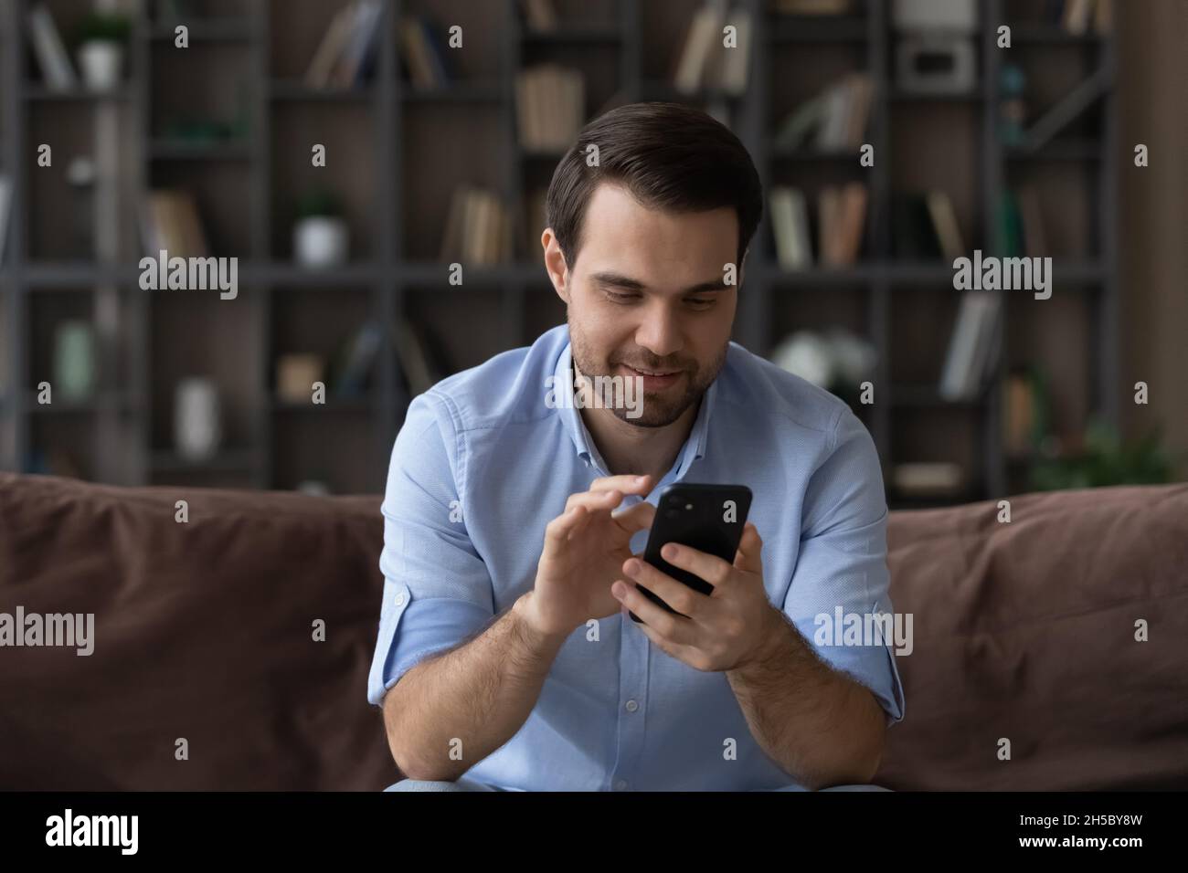 Smiling young man enjoying using mobile application. Stock Photo