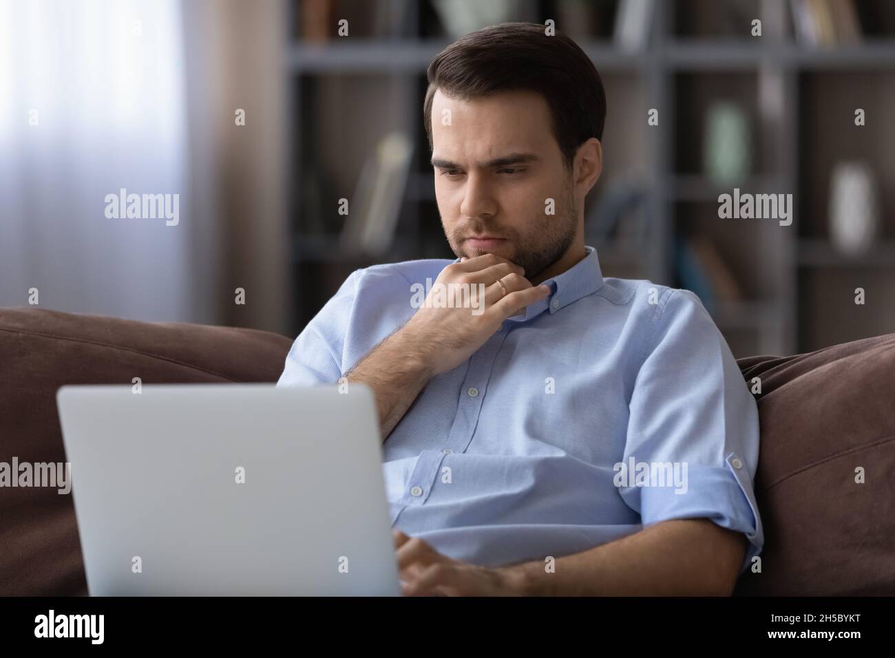 Thoughtful young man looking at laptop screen. Stock Photo