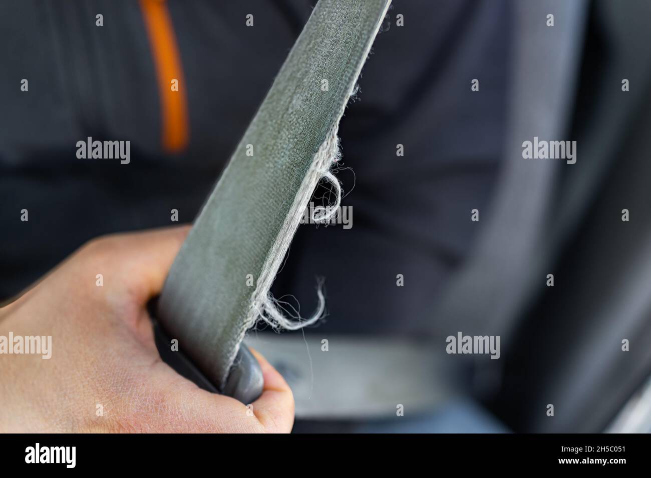 Macro closeup of man driver or passenger holding pulling old frayed ripped torn damaged car vehicle seat belt or seatbelt Stock Photo