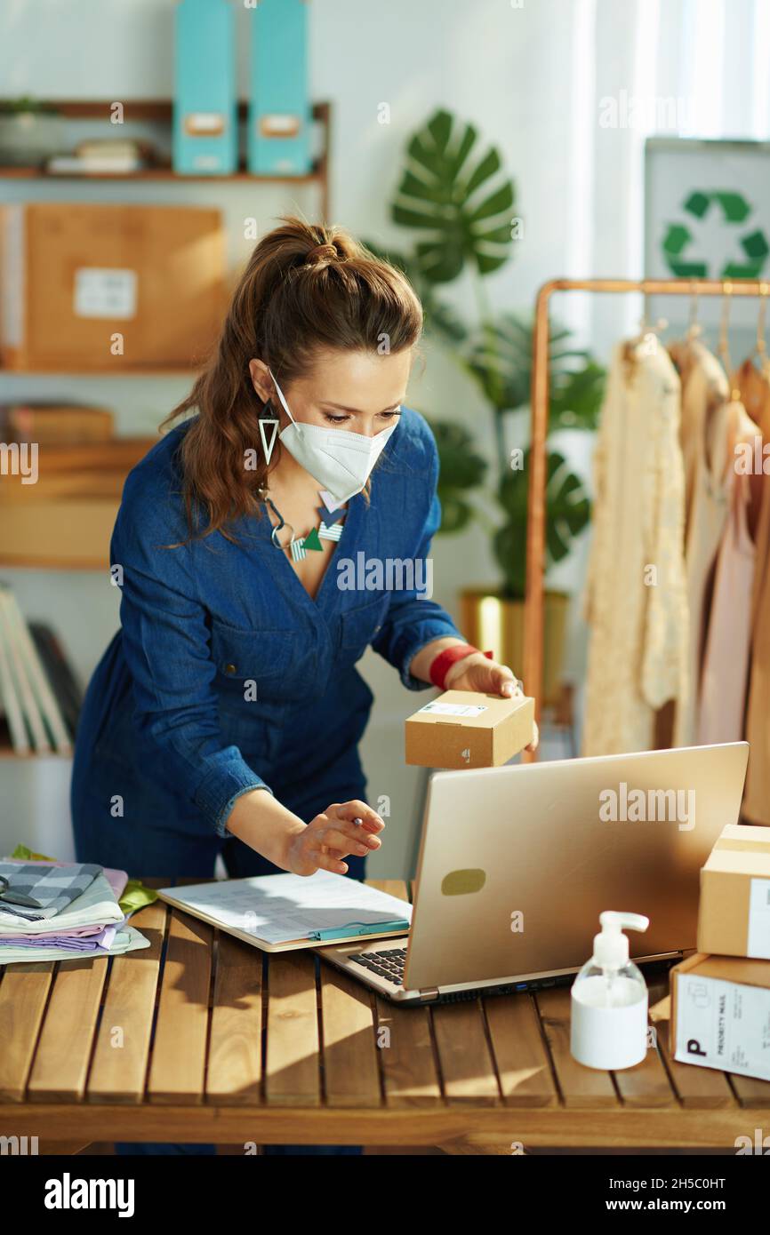 stylish 40 years old small business owner woman with ffp2 mask and an antibacterial agent using laptop in the office. Stock Photo