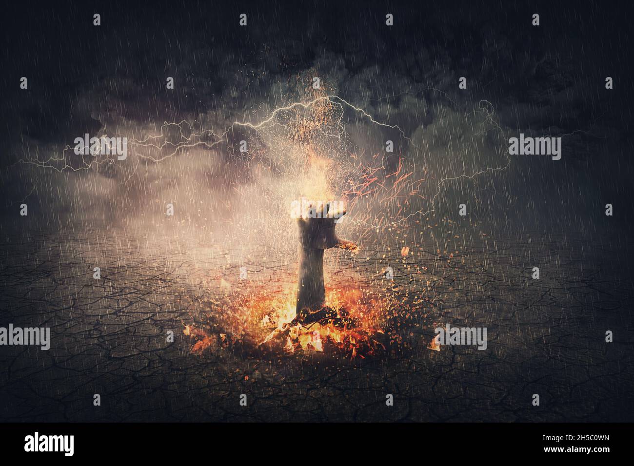 Hand on fire rising out from the ground. Surreal scene with flaming demon arm getting out of hell. Halloween concept, spooky background Stock Photo