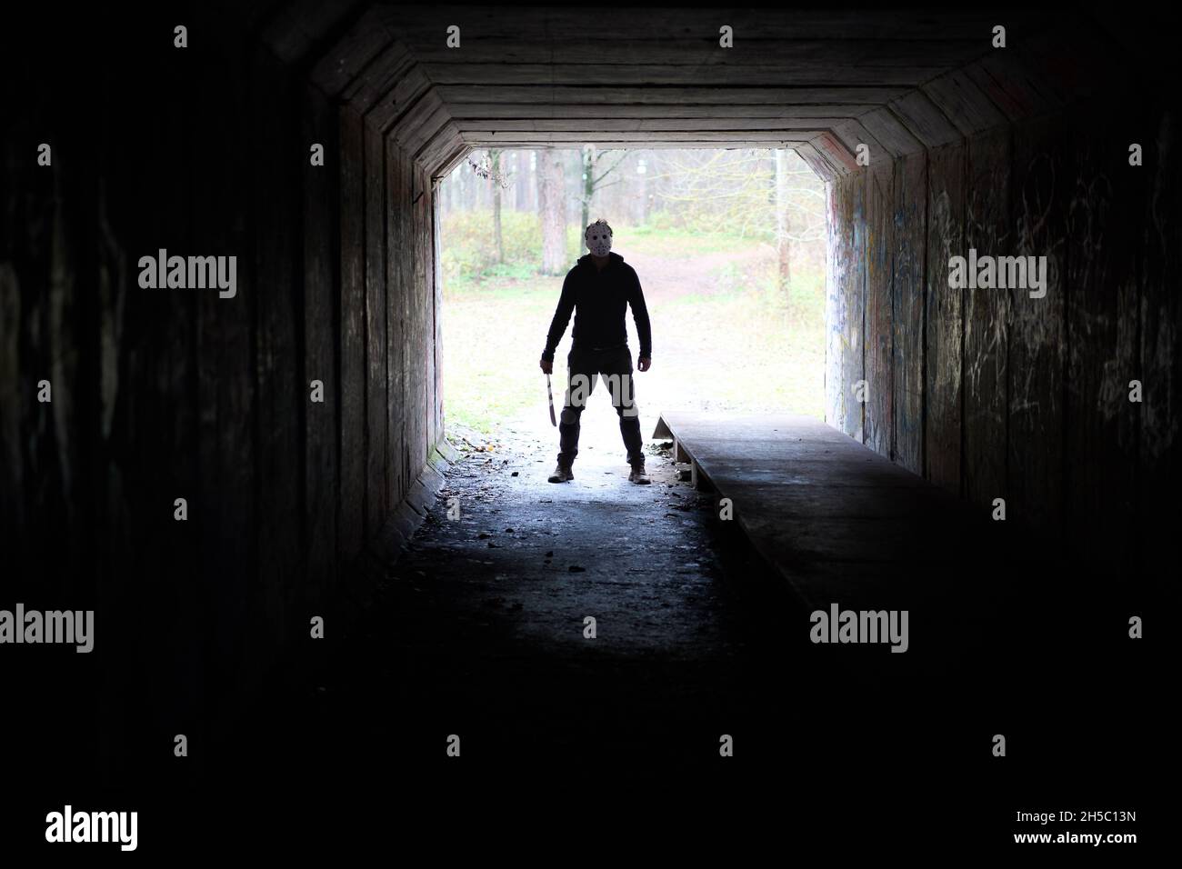 Serial killer Jason Voorhees in hockey mask and machete in the end of the dark tunnel. Friday 13h cosplay costume.  Stock Photo