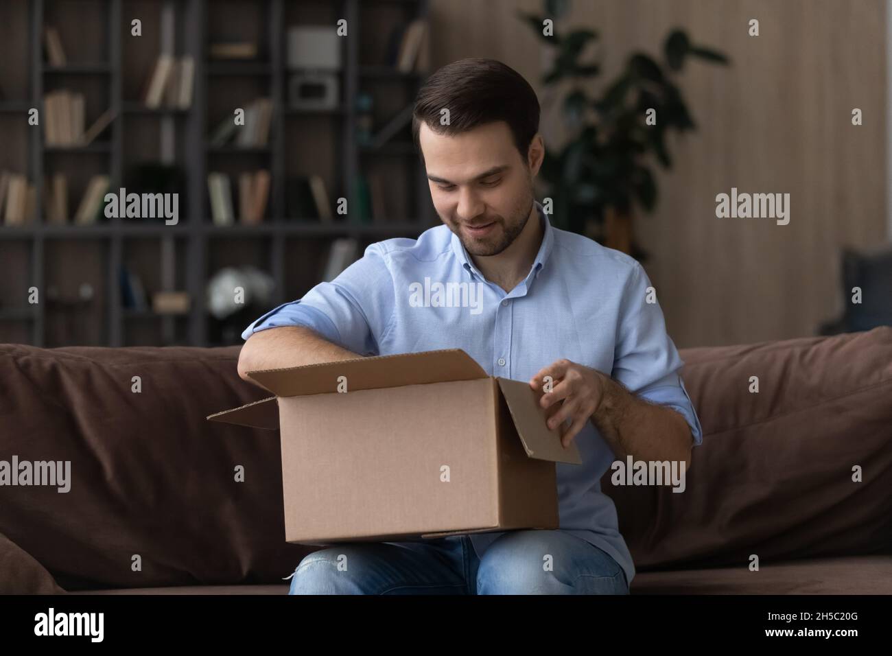 Interested young man unpacking big carton box, Stock Photo