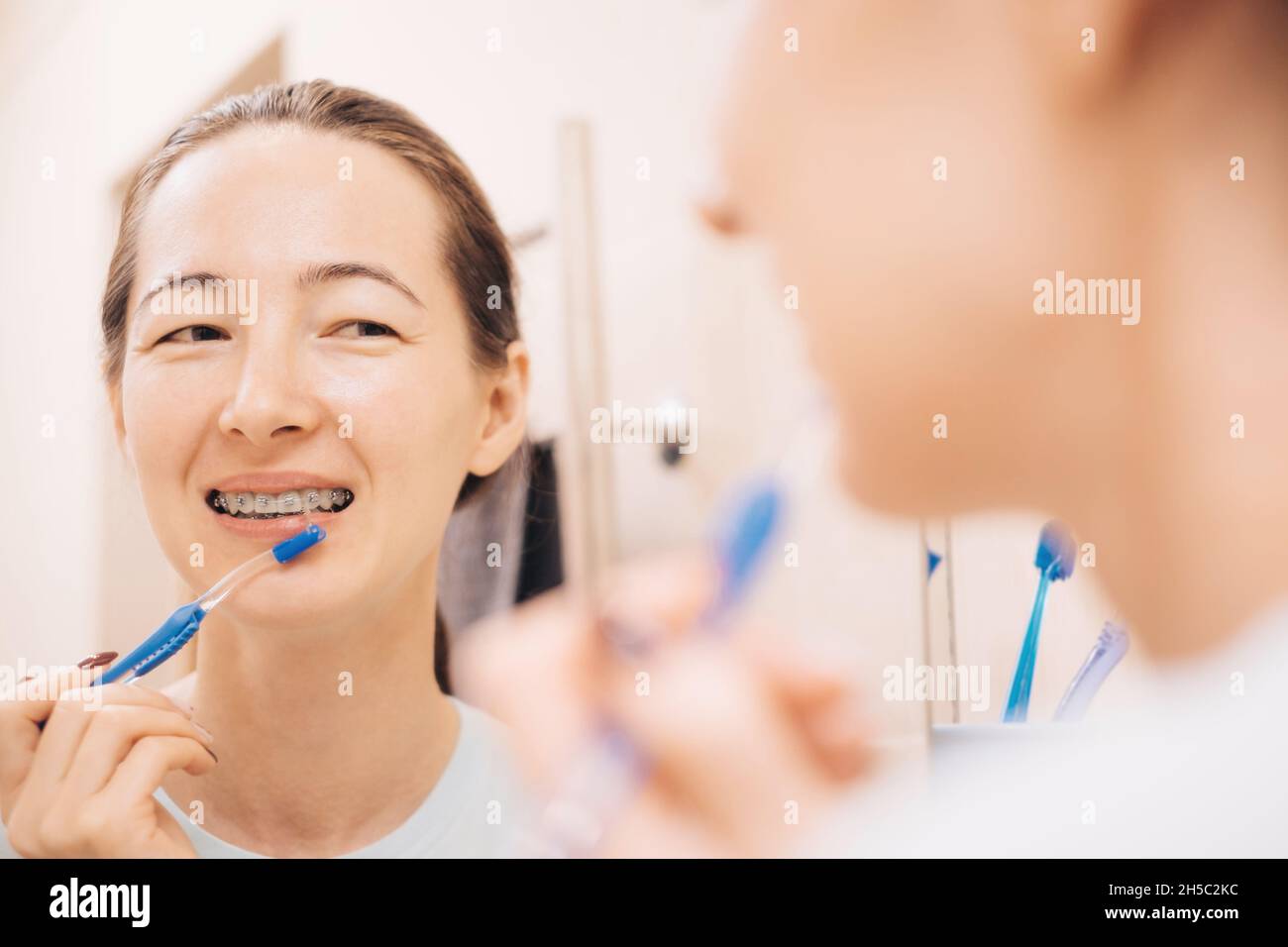 Young woman with braces on her teeth brushing her teeth with a special dental brush, before