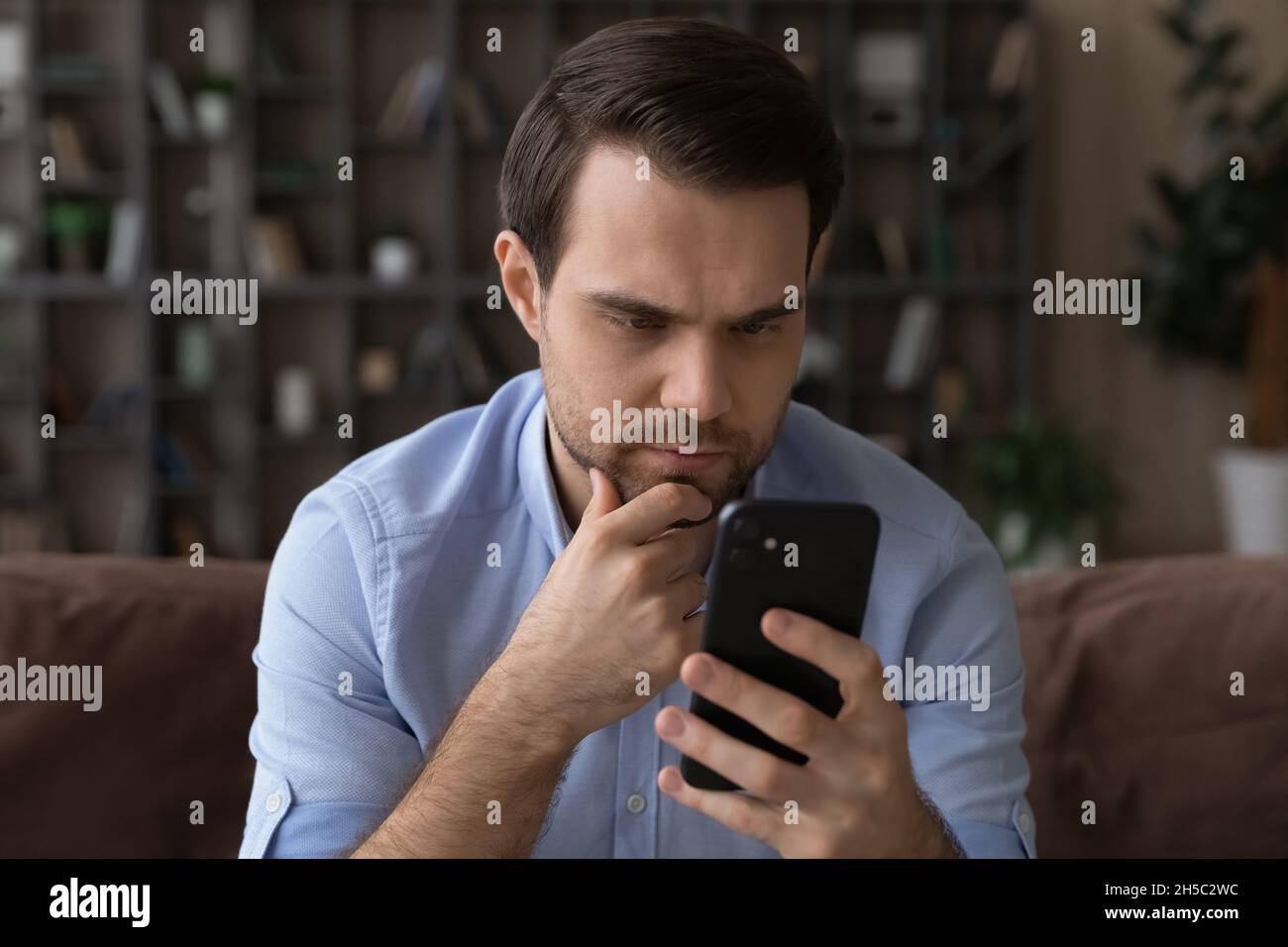 Thoughtful young man looking at cellphone screen. Stock Photo
