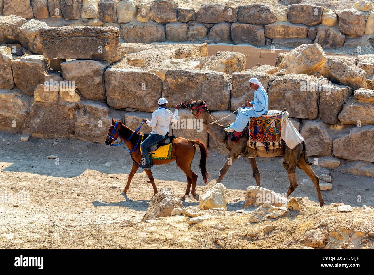 GIZA, EGYPT - JULY 14, 2021: A man on a camel and a man on a horse near the Great Pyramid in Giza, Egypt Stock Photo