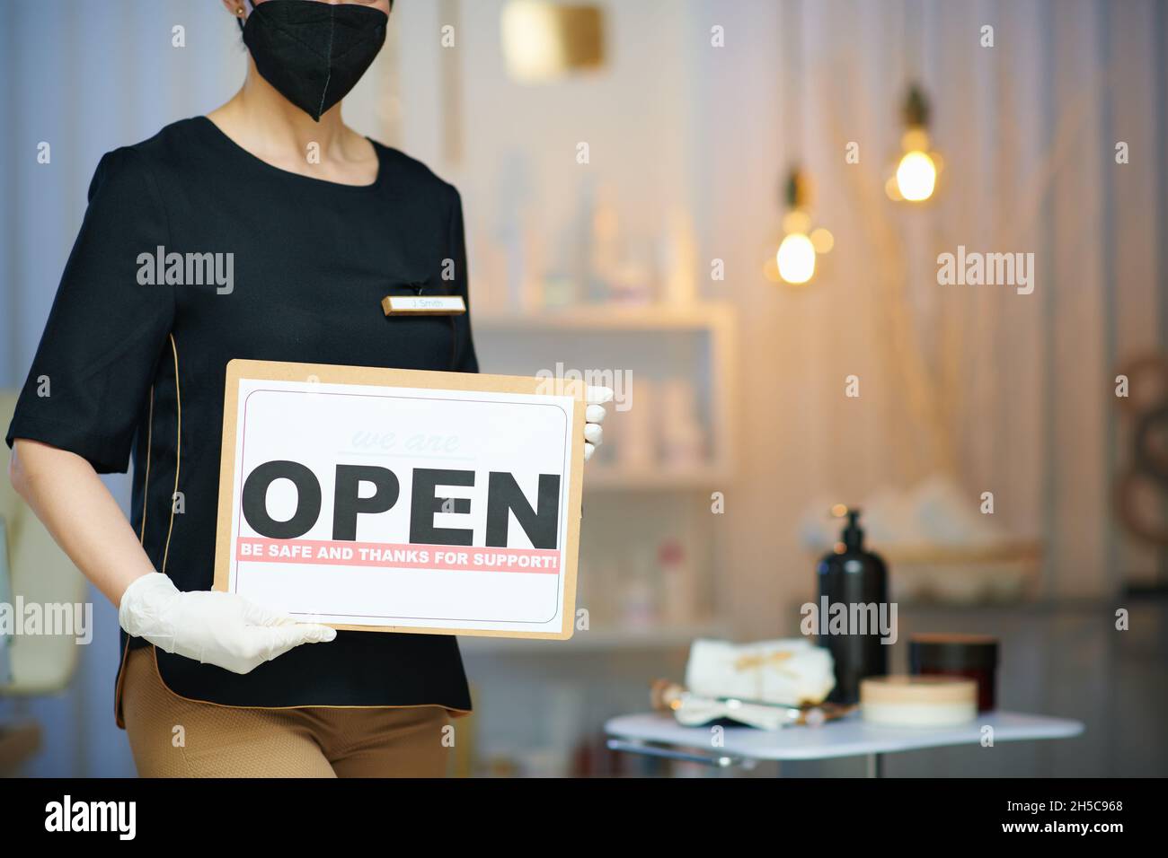 Business during coronavirus pandemic. Closeup on woman worker with ffp2 mask and open sign in modern beauty studio. Stock Photo
