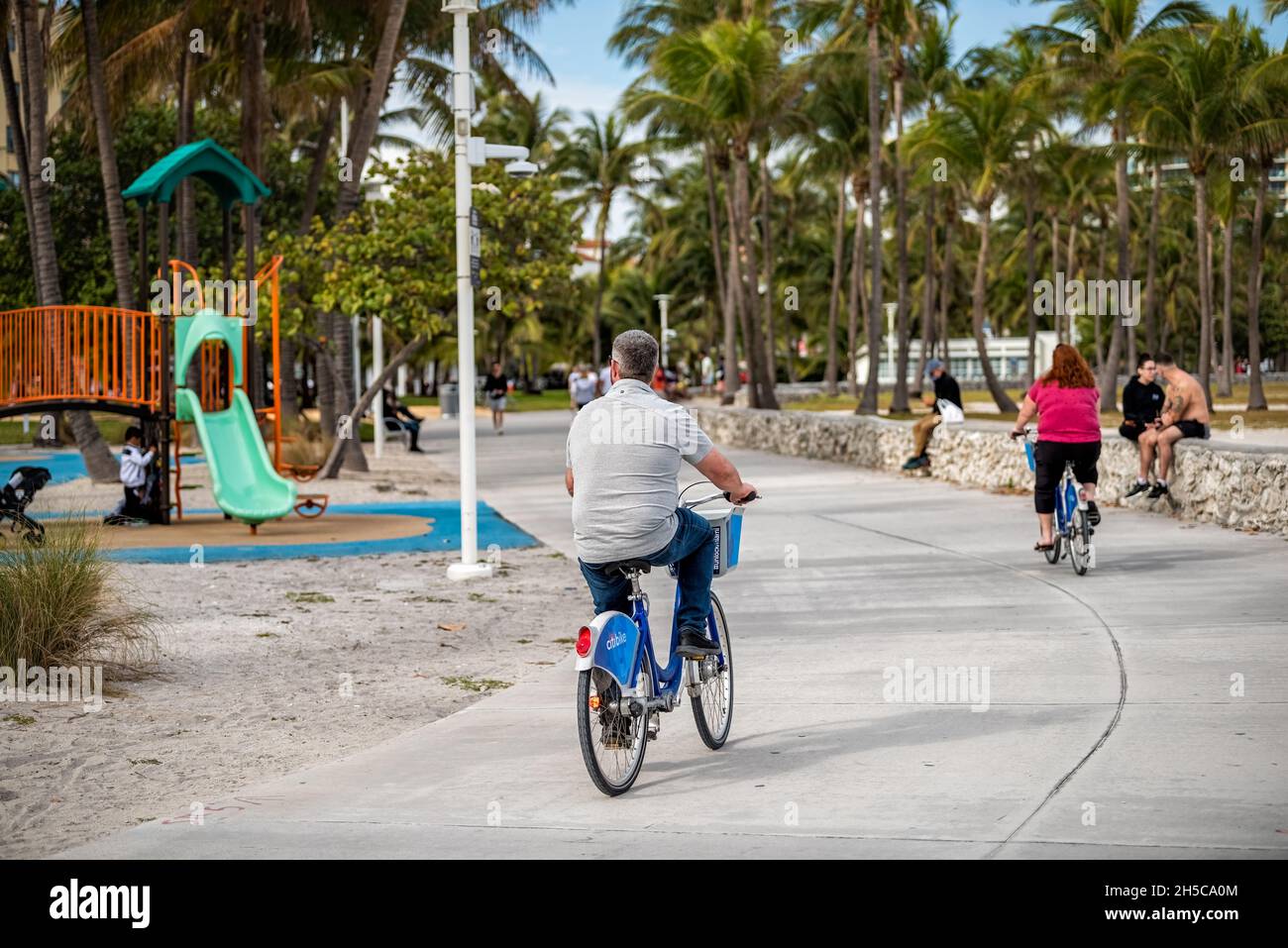Miami Beach, USA - January 17, 2021: People riding bicycles on ocean walk boardwalk at Lummus public park by Ocean drive in art deco district of South Stock Photo
