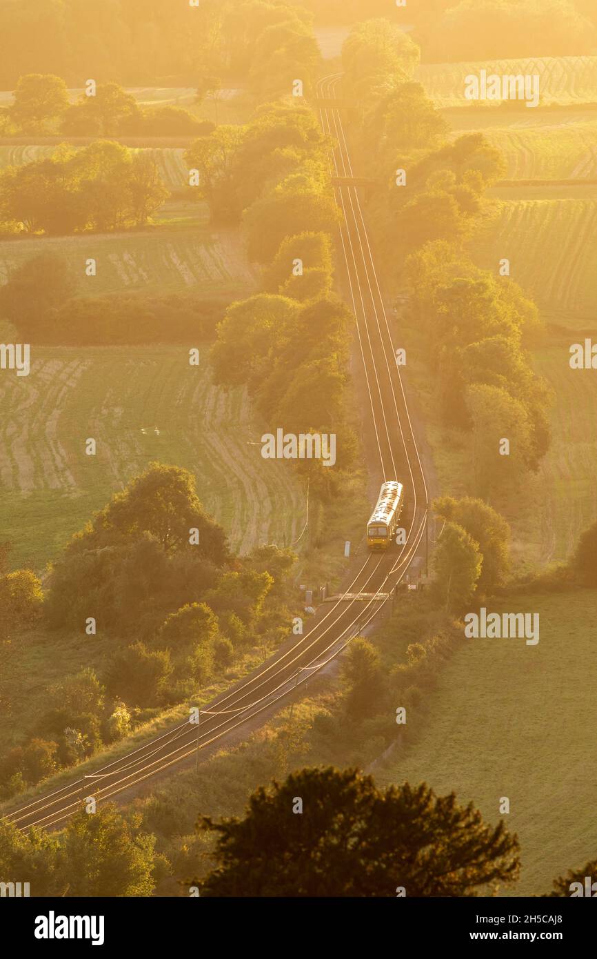 Train travelling through English countryside, Surrey, evening light, high viewpoint, North Downs Line. Sunlight shining on rails Stock Photo