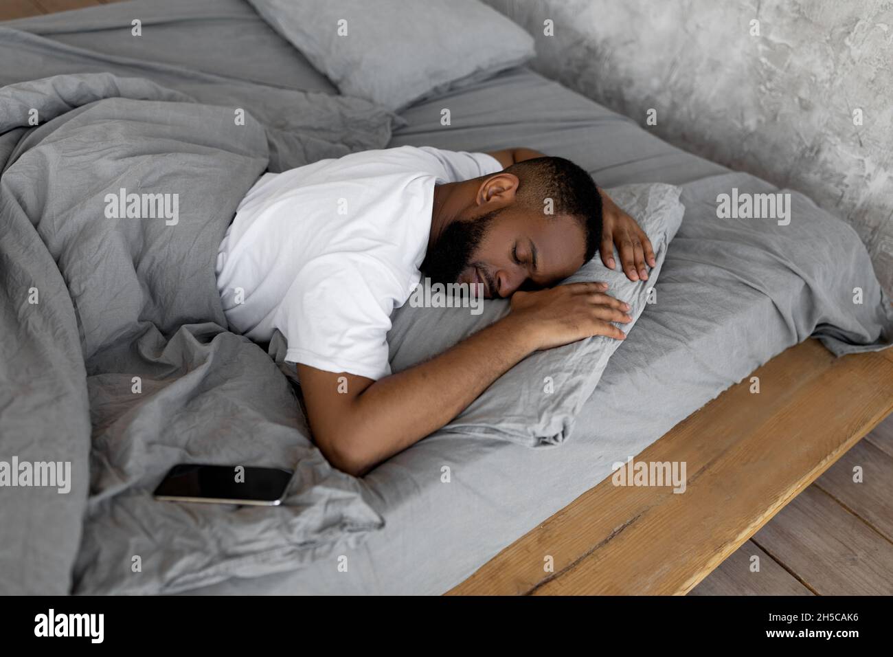 Young African American man sleeping in bed with cellphone Stock Photo