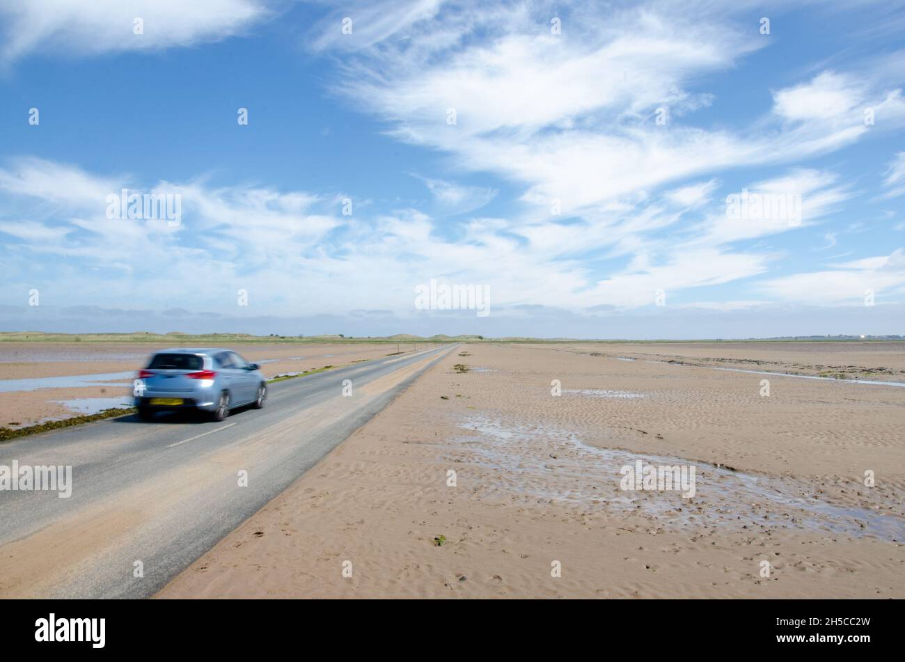 Car on causeway at low tide leading to Lindisfarne Castle on Holy Island, off the Northumberland coast in the north east of England, UK. Stock Photo