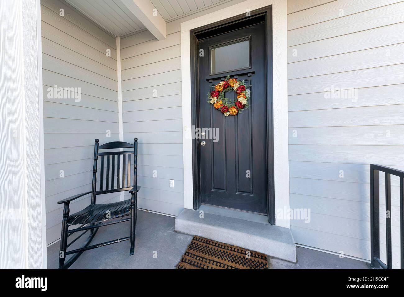 Small porch of a traditional house with black front door with wreath and black rocking chair Stock Photo