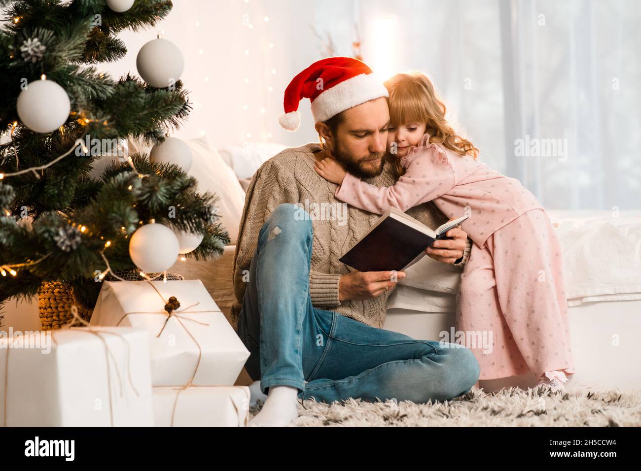 Father in santa hat reads a fairy tale to his beloved daughter Stock Photo