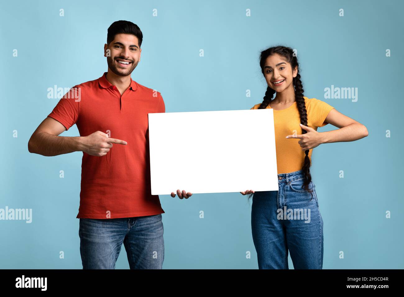Nice Offer. Cheerful Arab Couple Pointing At White Blank Placard In Hands Stock Photo