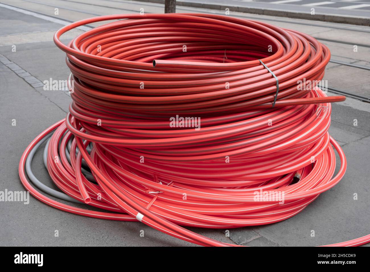 Rolled up red flexible plastic pvc tubing tube heap for covering new cables underground on the street near a construction site in europe. Stock Photo