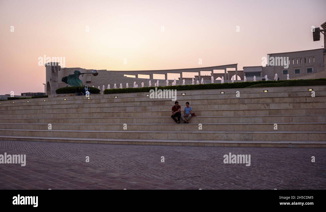 The amphitheater in Katara Cultural Village, Doha , Qatar panoramic view at sunset with Force of Nature 2 statue and  people sitting and walking Stock Photo