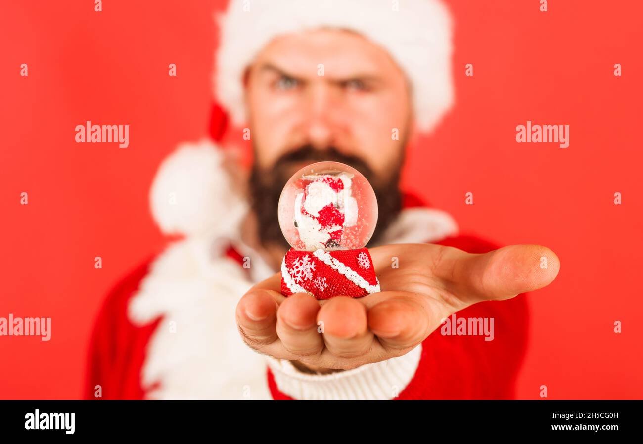 Man in Santa costume with small snow globe. Christmas snow globe. New Year and Christmas decorations. Selective focus. Stock Photo
