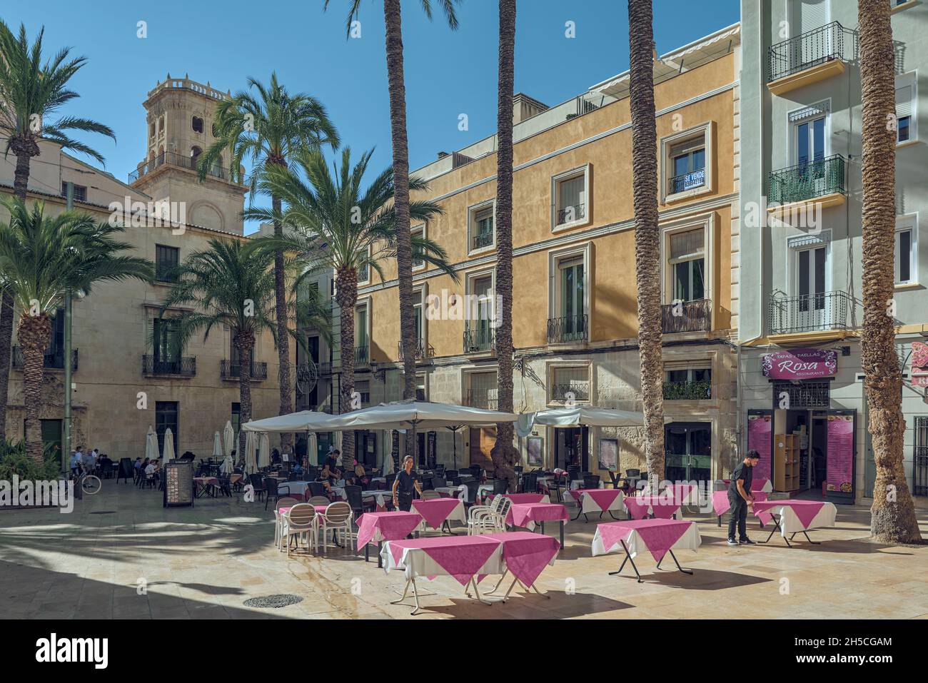 terraces with chairs and tables with their red tablecloths of the bars in the Plaza de la Santísima Faz behind the town hall of the city of Alicante Stock Photo